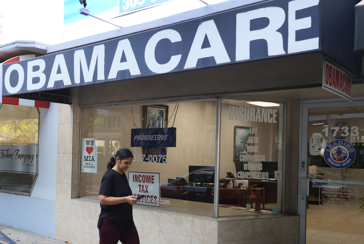 A pedestrian on their phone walks by an obamacare sign