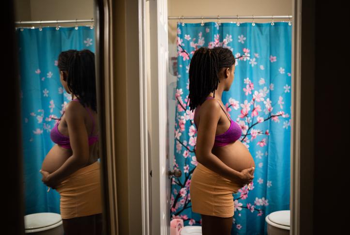 Black pregnant woman stands in bathroom holding stomach