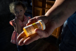 Hand holds out prescription bottle in front of young girl