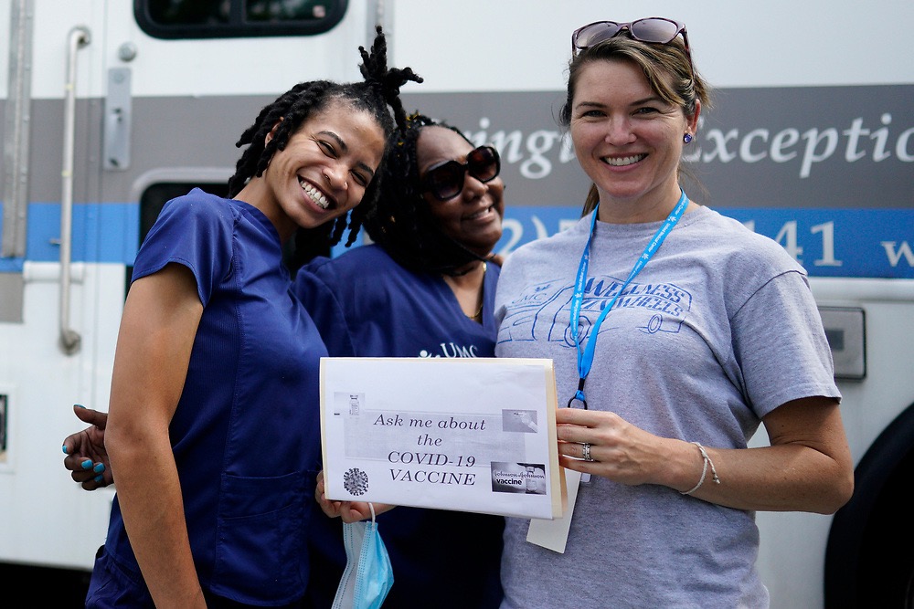 Nurse and managers of the mobile clinic pose for photo with sign