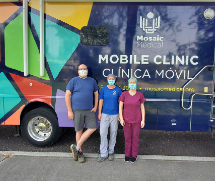 three health workers in masks stand in front of mobile clinic van