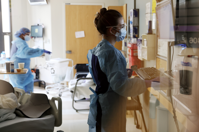 Nurse in full PPE works on computer in ICU.