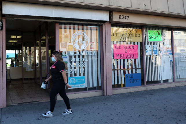 Woman in mask walks by clinic window with signs in Spanish