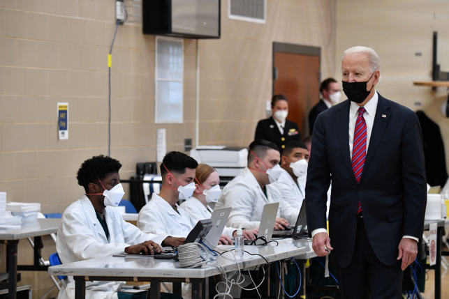 Photo, President Biden walking past health technicians wearing masks