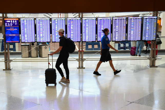 A Transportation Security Administration (TSA) officer walks past an airline passenger not wearing a face mask in an airport