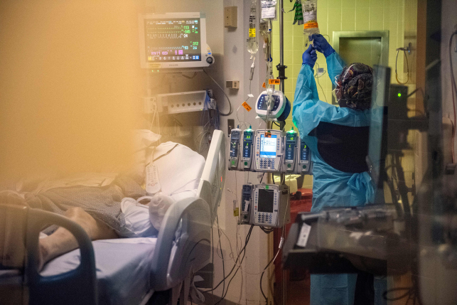 hospital worker changes IV bag next to patient in hospital bed