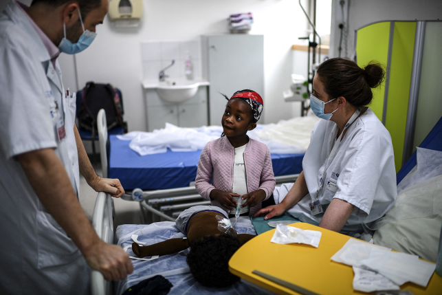 Girl sits on hospital bed with two hospital staffers