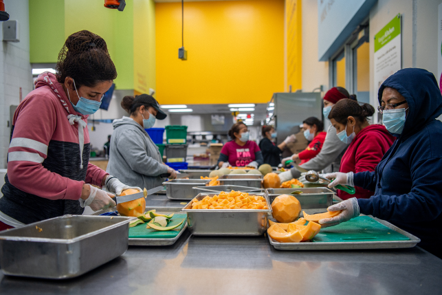 Volunteers in masks prepare fruit at a long table in a food bank