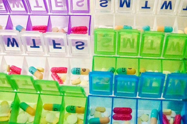 Aerial view of brightly colored pill boxes for days of the week open with pills in each box