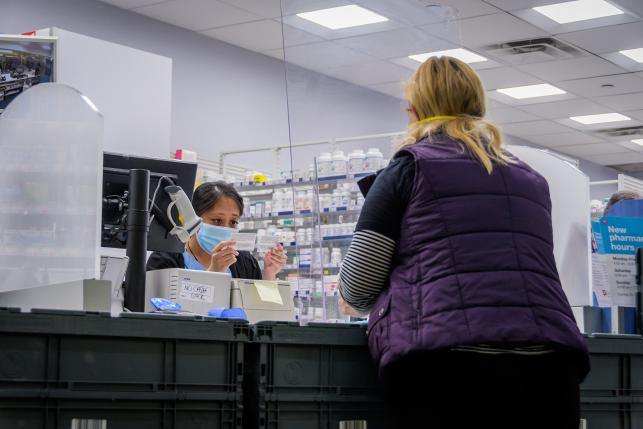 Pharmacy attendant wearing a face mask while checking a patients insurance card