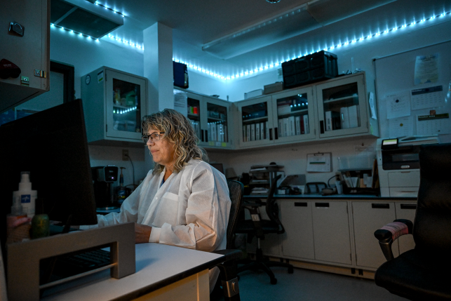 Tech in front of computer in white lab coat.
