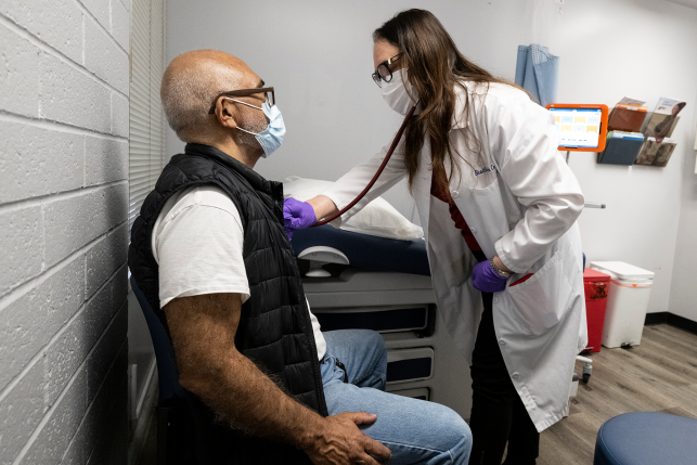Doctor in mask examines seated patient in mask