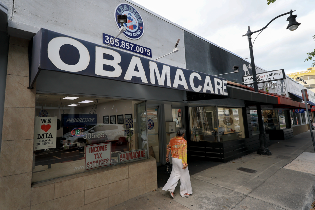 Woman walks in front of storefront that reads Obamacare