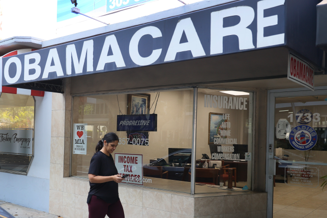 A pedestrian on their phone walks by an obamacare sign