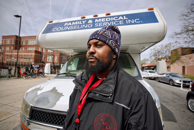 Man in hat stands in front of Familly and Medical Counseling Service bus