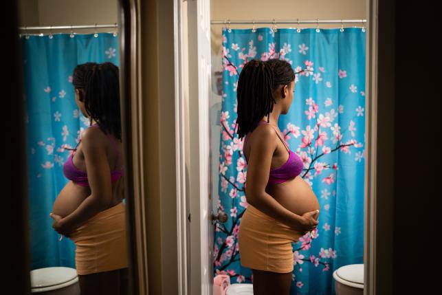 Black pregnant woman stands in bathroom holding stomach