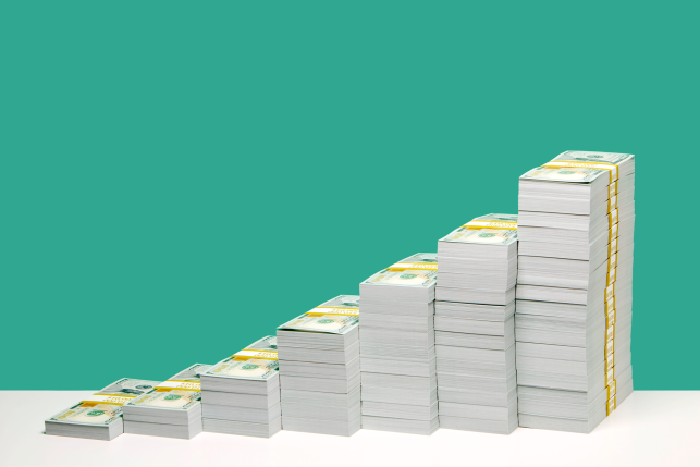 Stacks of U.S. hundred dollar bill bundles in ascending order on white shelf, green background.