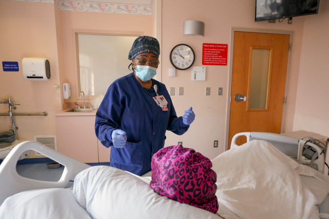 Photo, nurse in mask talks to patient in bed