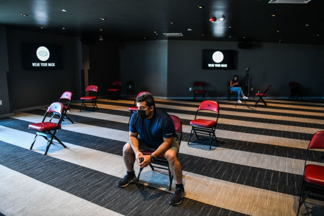 Masked man sits alone on red chair in empty room with chairs spaced apart