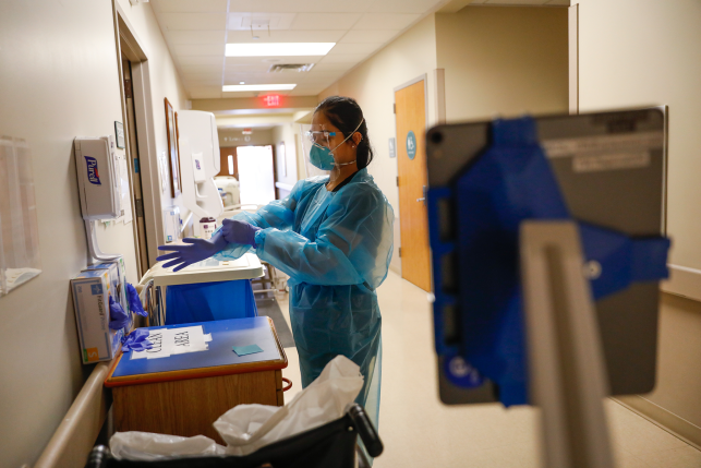 Photo, nurse puts on gloves while wearing full PPE