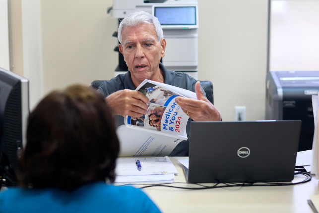 Man opens brochure for woman in front of computer