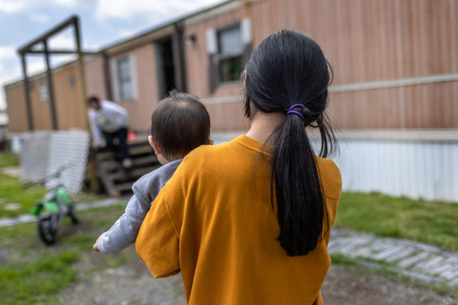 Photo, back of girl holding baby in front of trailer