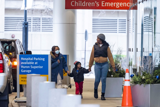 Photo, three people walk past hospital sign