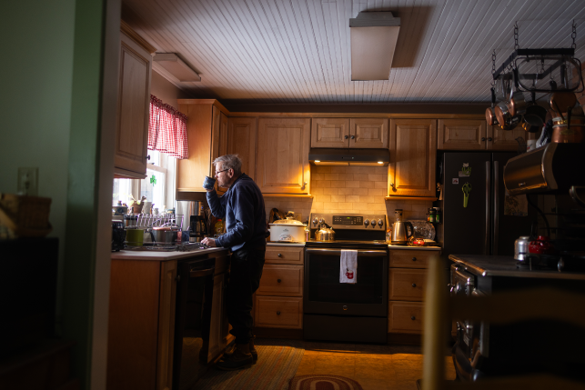 Elderly man drinking from coffee cup staring out kitchen window