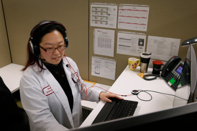Woman in lab coat and headset talks while using computer