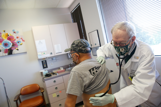 Doctor examines patient in doctors office while both wear masks