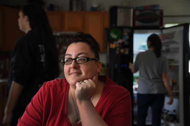 Woman sits in a dark kitchen surrounded by children looking contemplative