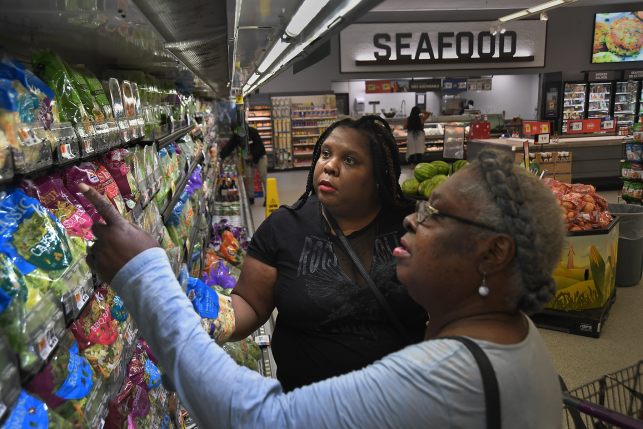 Two women in grocery store look at bagged lettuce