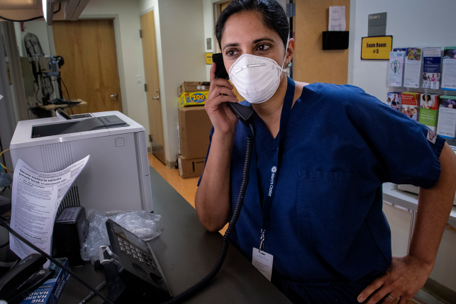Female physician in scrubs and mask on phone in hospital