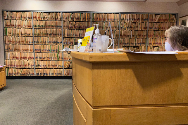 Receptionist sitting at desk next to wall of medical records