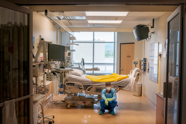 Photo, nurse in full PPE bends down in front of empty hospital bed