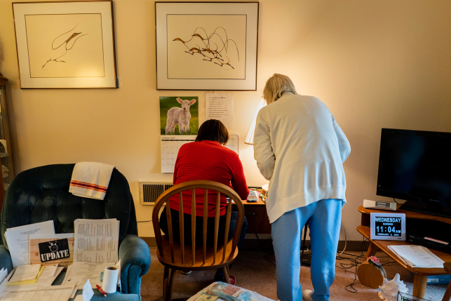 Photo, two women huddle over computer in room