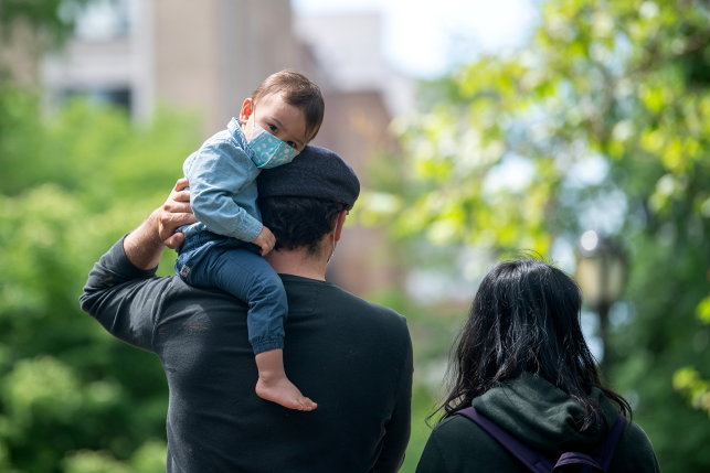 Father with child on shoulders in mask walks with wife in park