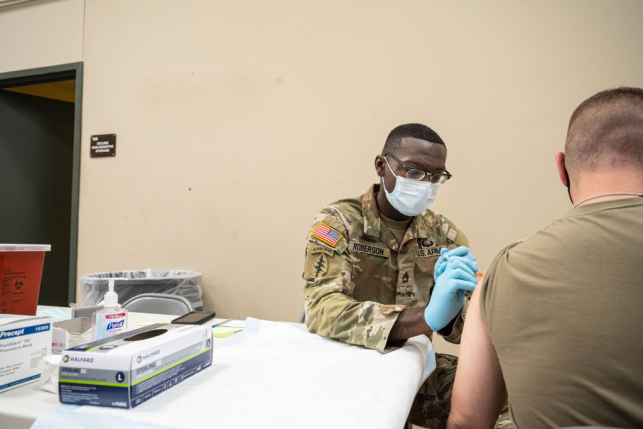Military doctor gives vaccine to other military member at white table
