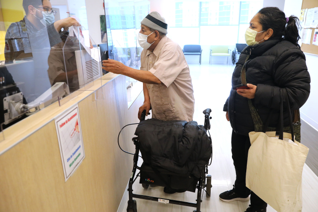 Man in mask with walker gets paperwork from clinic desk.