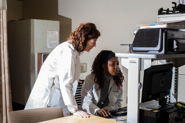 Two lab coat-wearing employees work on computer