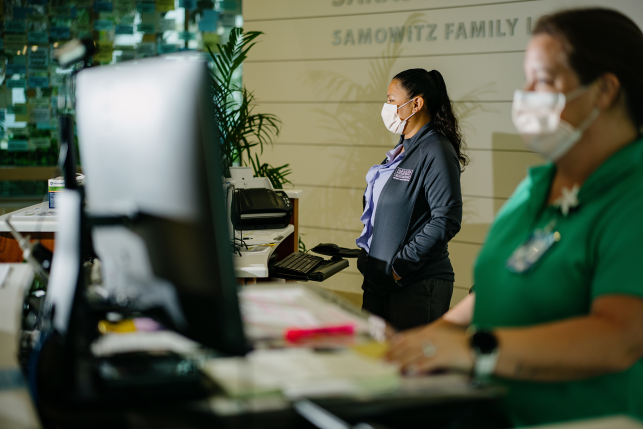 Two women in masks stand at computers