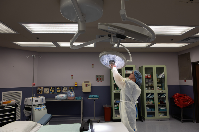 Medical professional turns on operating light in operation room.