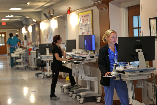 Medical professionals work at computers in hospital corridor
