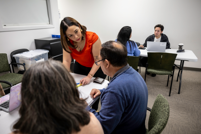 Woman leans over table and paperwork while talking to man