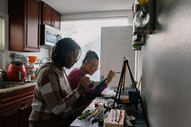 Photo, two women at easel in kitchen.