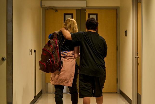Teenager has arm around mom while they walk down a hospital hallway