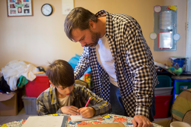 Man helps young boy with homework at a table.