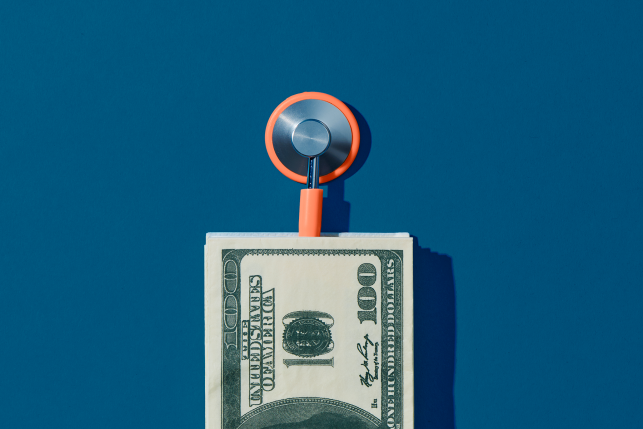 Photograph of stethoscope coming out of a pile of hundred US dollar bills