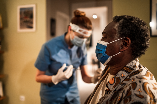 Elderly woman in mask waiting for nurse with vaccine in home