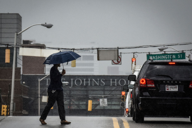 Pedestrian crosses with umbrella in front of Johns Hopkins hospital